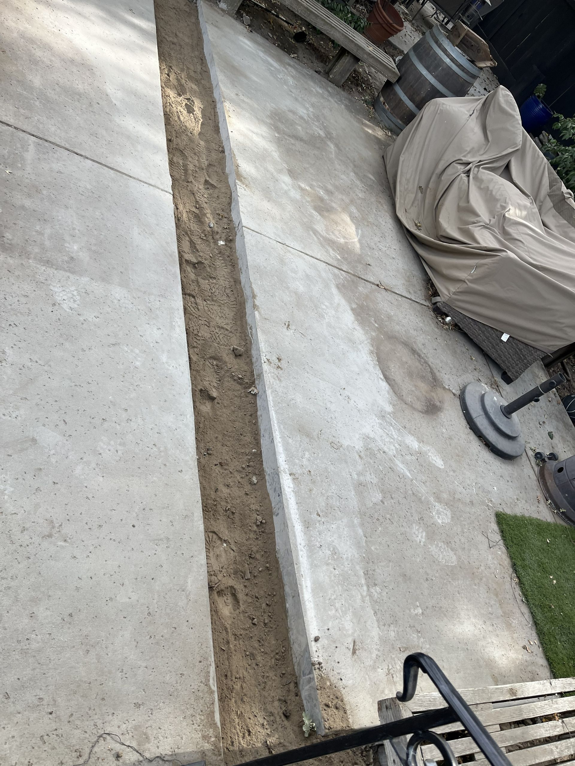 A concrete patio featuring a long, narrow trench cut through the center, filled with dirt.