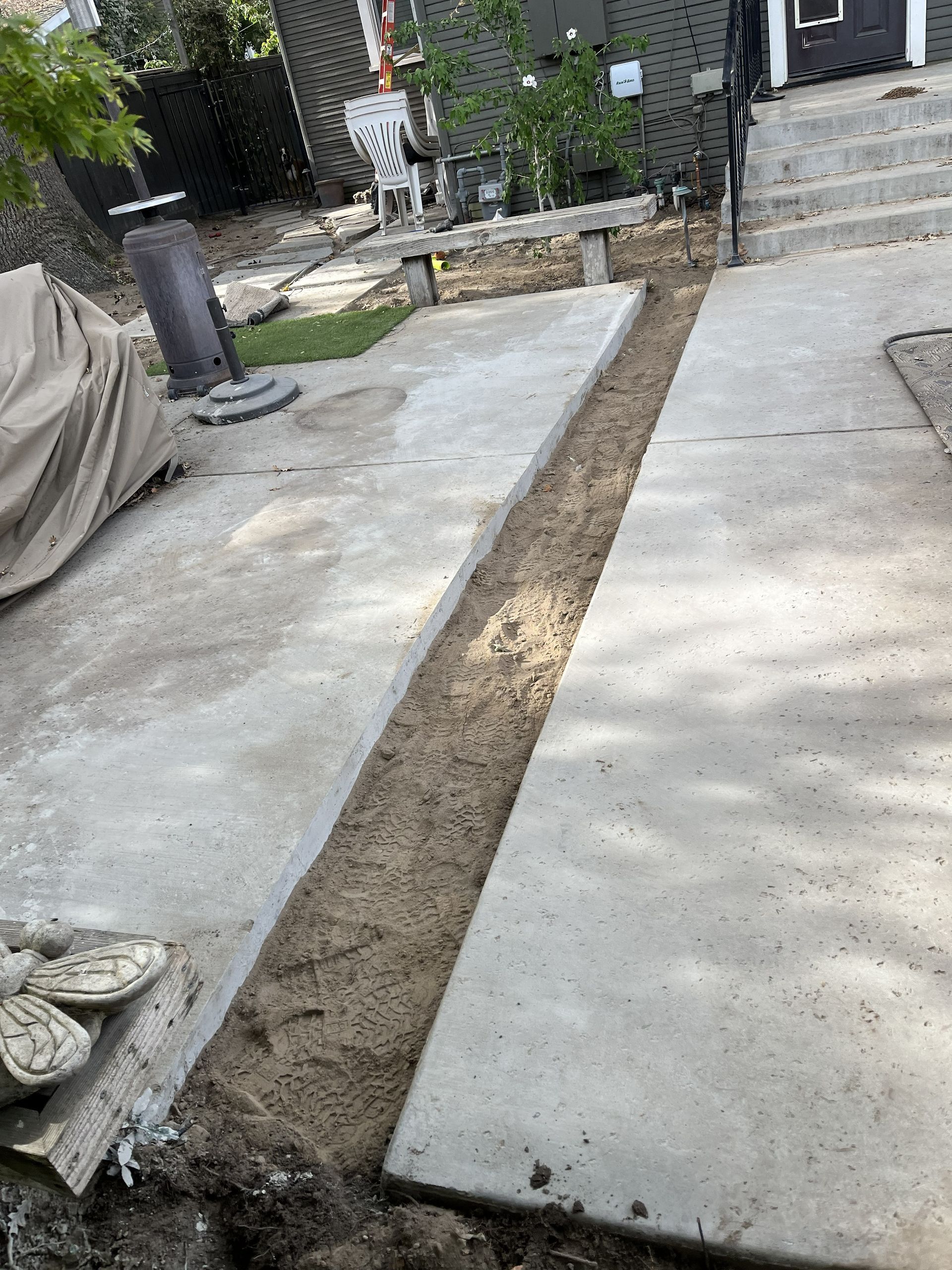 A ground-level view of a concrete driveway with a long, narrow trench of exposed dirt running through the middle.
