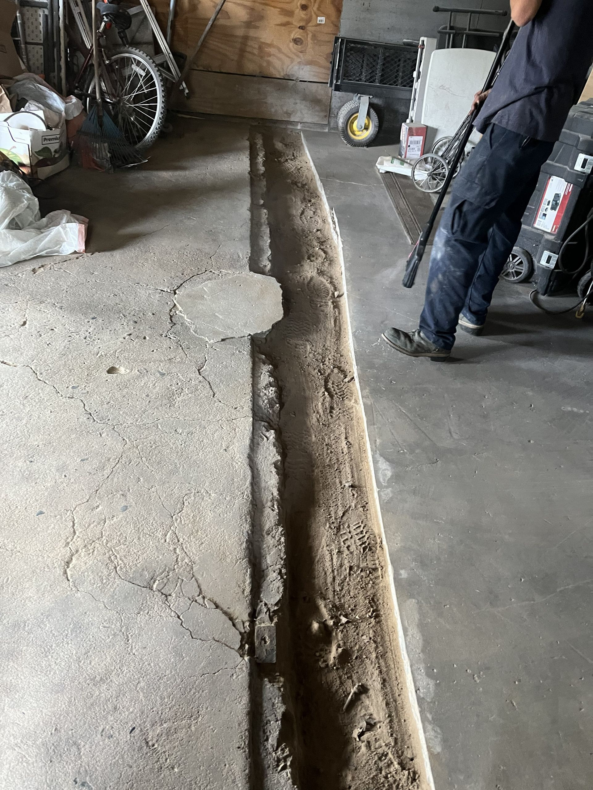 A person stands in a garage next to a long, rectangular trench cut into the concrete floor.