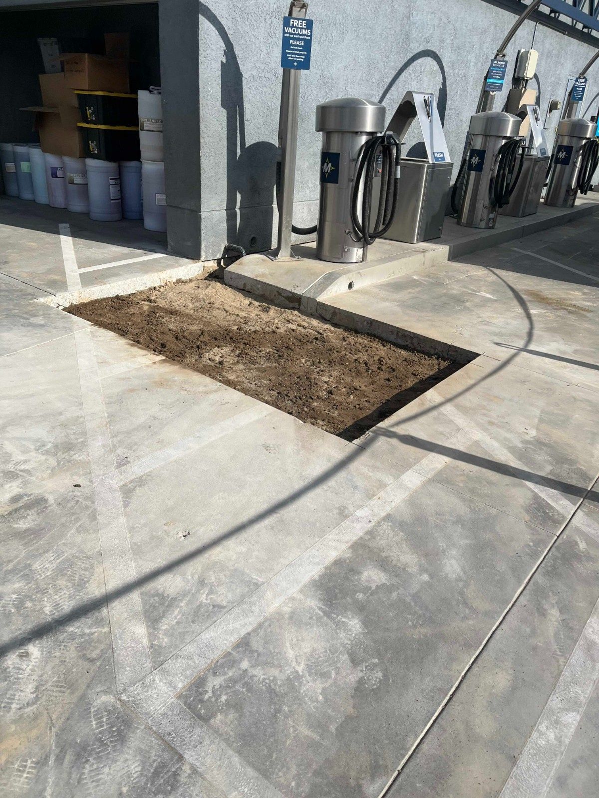 A rectangular patch of dirt exposed in a concrete ground, located next to several upright car wash vacuum stations.