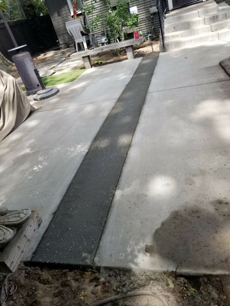 A dark, textured rubber ramp strip installed on a concrete patio leading toward a set of outdoor stairs.