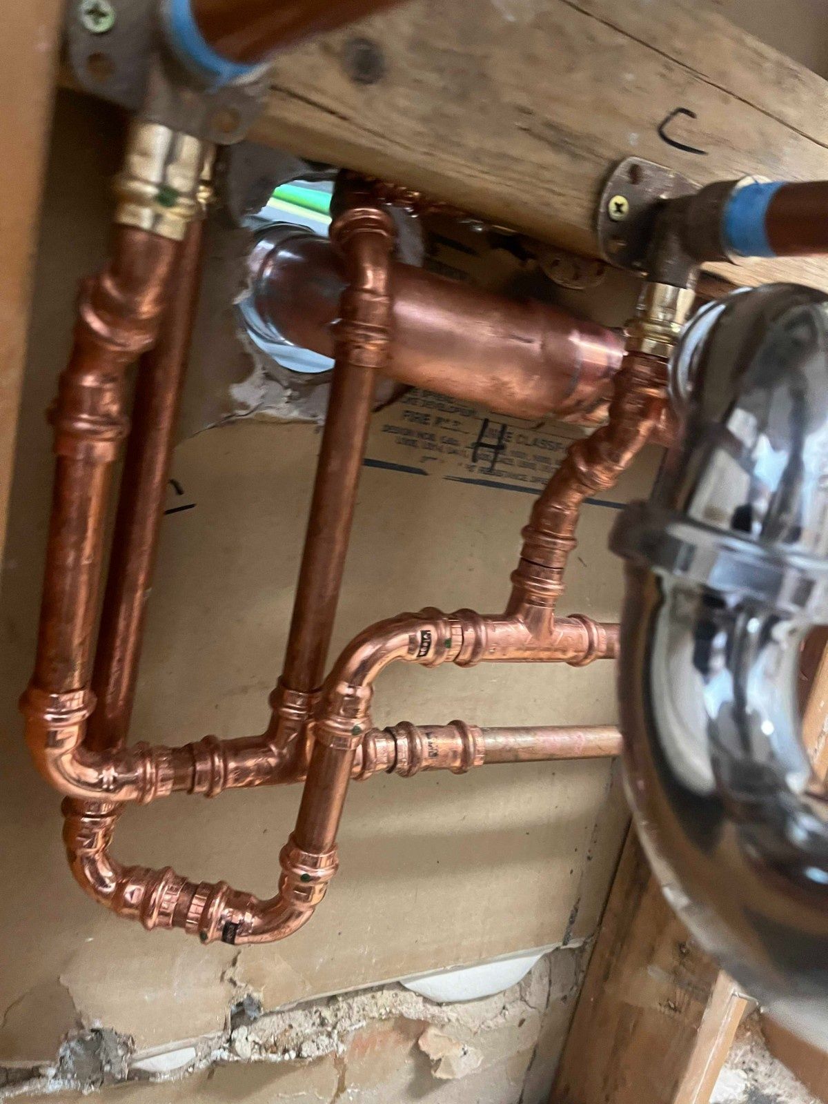 A close-up view of copper plumbing pipes and a chrome P-trap installed under a sink.