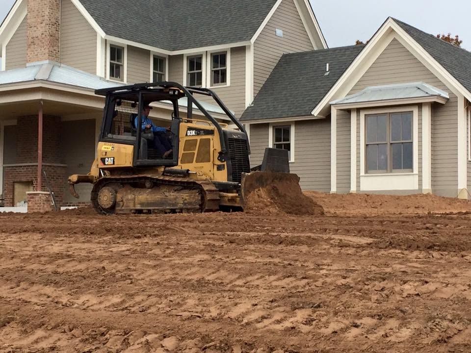 Yellow skid steer moving dirt in front of a suburban house during landscaping work
