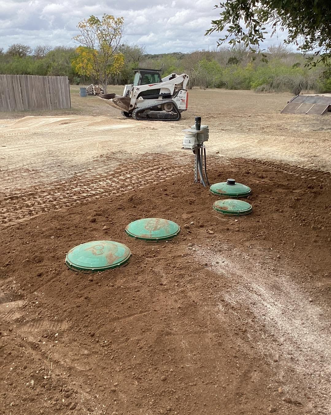 Dirt bike obstacle course with green mounds and a parked skid steer in a dusty outdoor field
