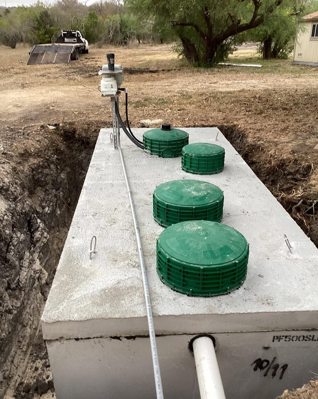 Concrete septic tank with four green access covers and pipe, in a dug-out yard area