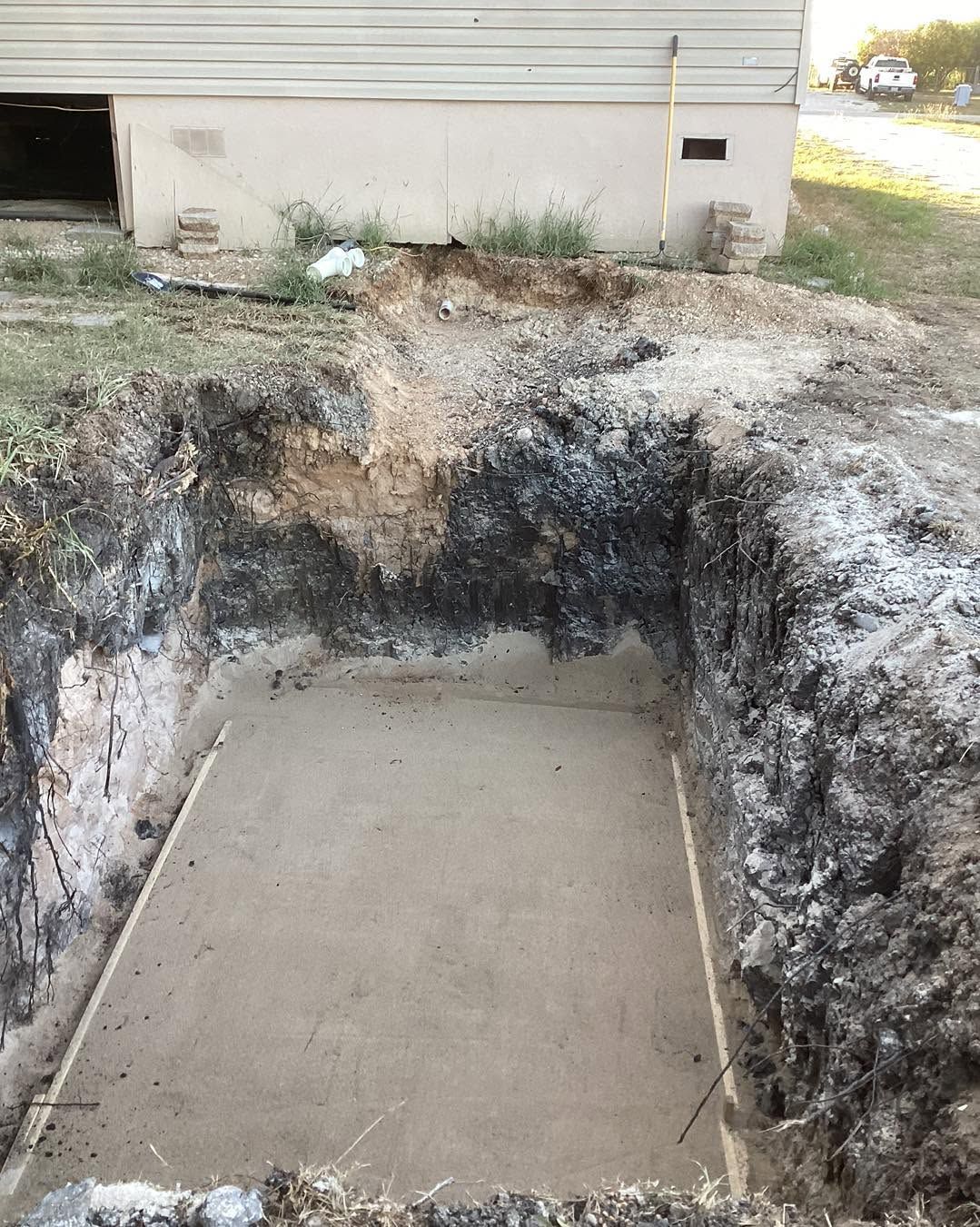 Freshly poured concrete slab in a large excavated hole beside a house exterior