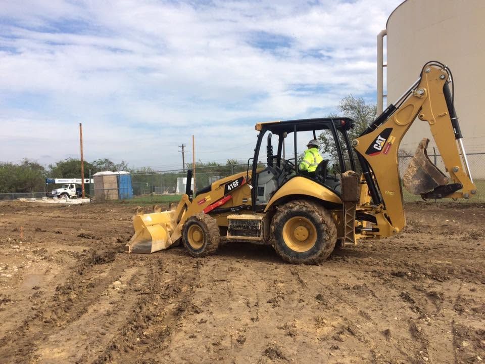 Yellow backhoe loader on a muddy construction site under a cloudy sky.