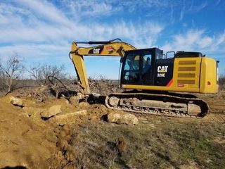 Yellow CAT excavator on a dirt hillside under a blue sky.
