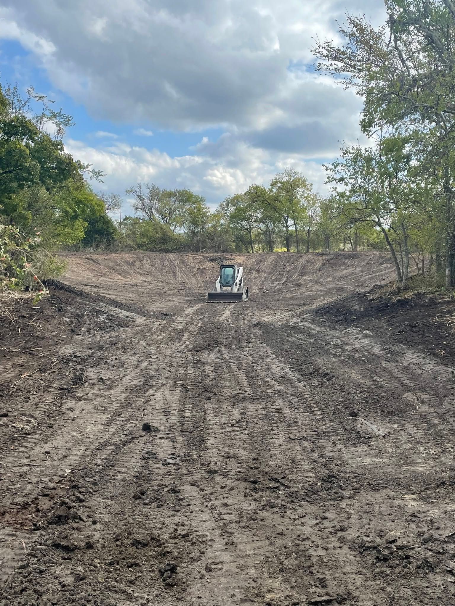 Bulldozer on a muddy dirt path between trees under a cloudy sky
