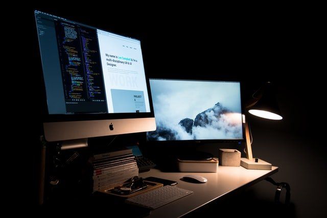 a desk with two computer monitors and a lamp on it
