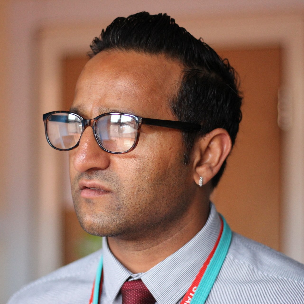 Man wearing glasses and a tie, looking to the side in an indoor office setting.