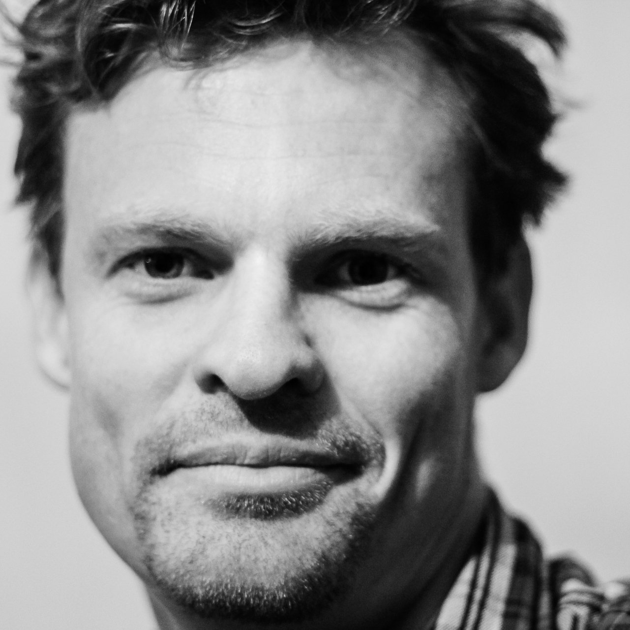 Close-up black-and-white portrait of a smiling man with tousled hair