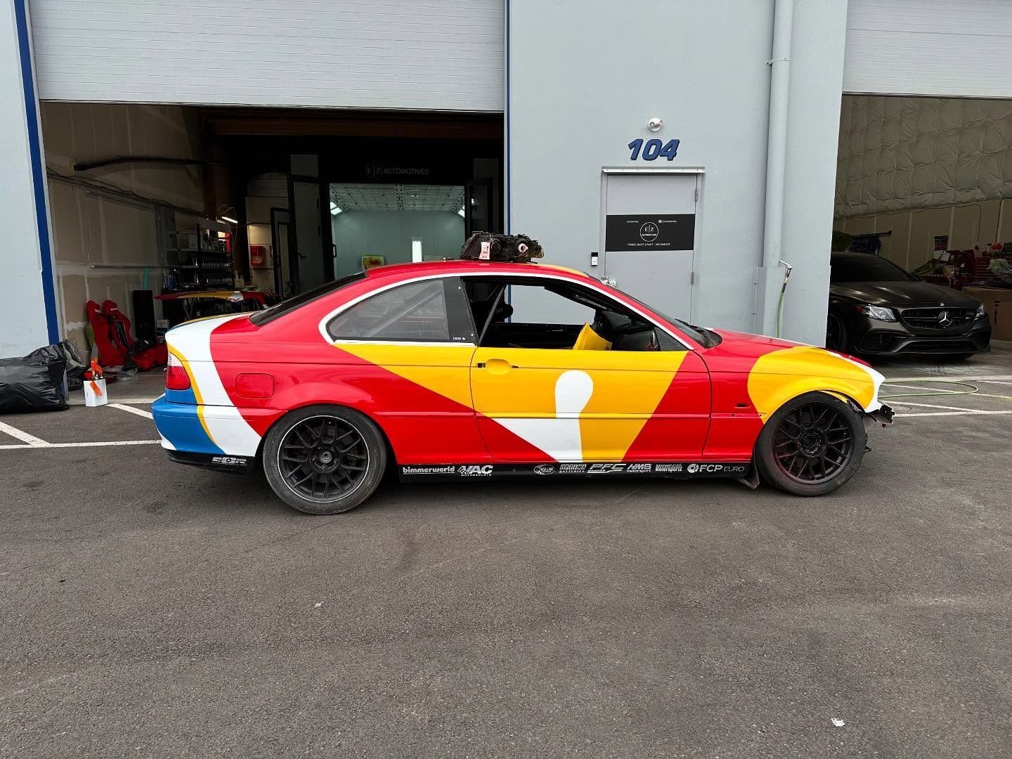 Red and yellow race car parked outside a garage with the number 106 above the door