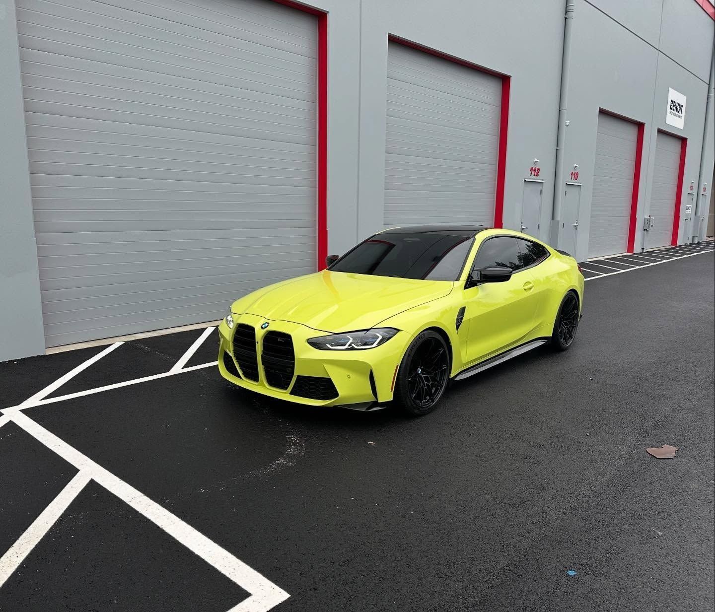 Bright yellow sports car parked outside gray warehouse doors on wet pavement