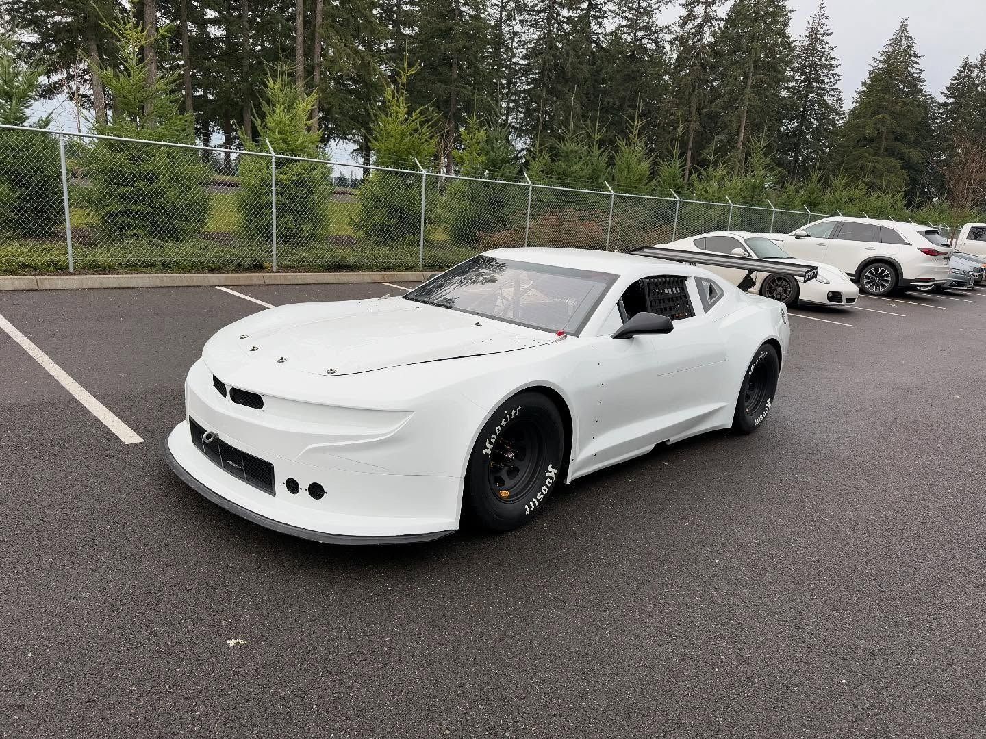 White sports car parked in a lot with several other cars and trees in the background