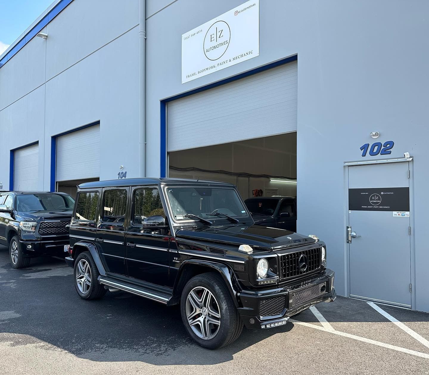 Black SUV parked outside a blue auto shop with open garage doors.
