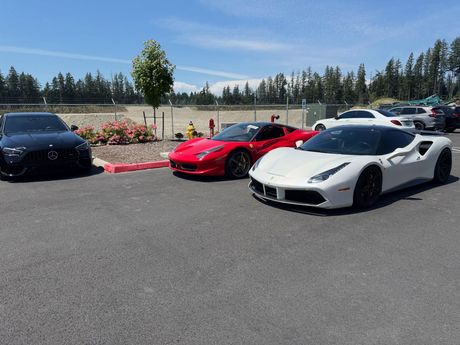 Three sports cars parked on an asphalt lot in bright sunlight, including a white car and a red car.