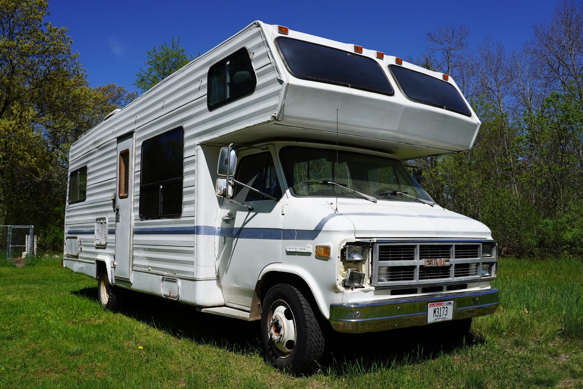 White camper van parked on grass under a blue sky, with trees in the background