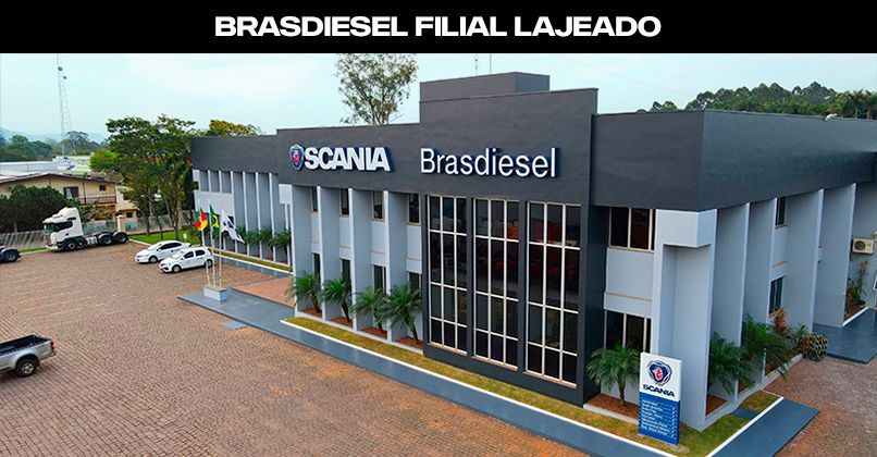 Vista aérea do moderno edifício cinza e preto da Scania Brasdiesel em Lajeado, com estacionamento pavimentado e bandeiras.