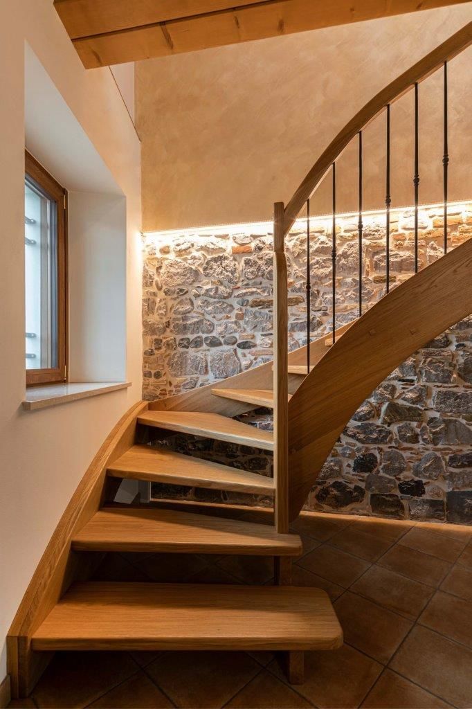 Una scala a chiocciola in legno in una stanza con un muro in pietra.