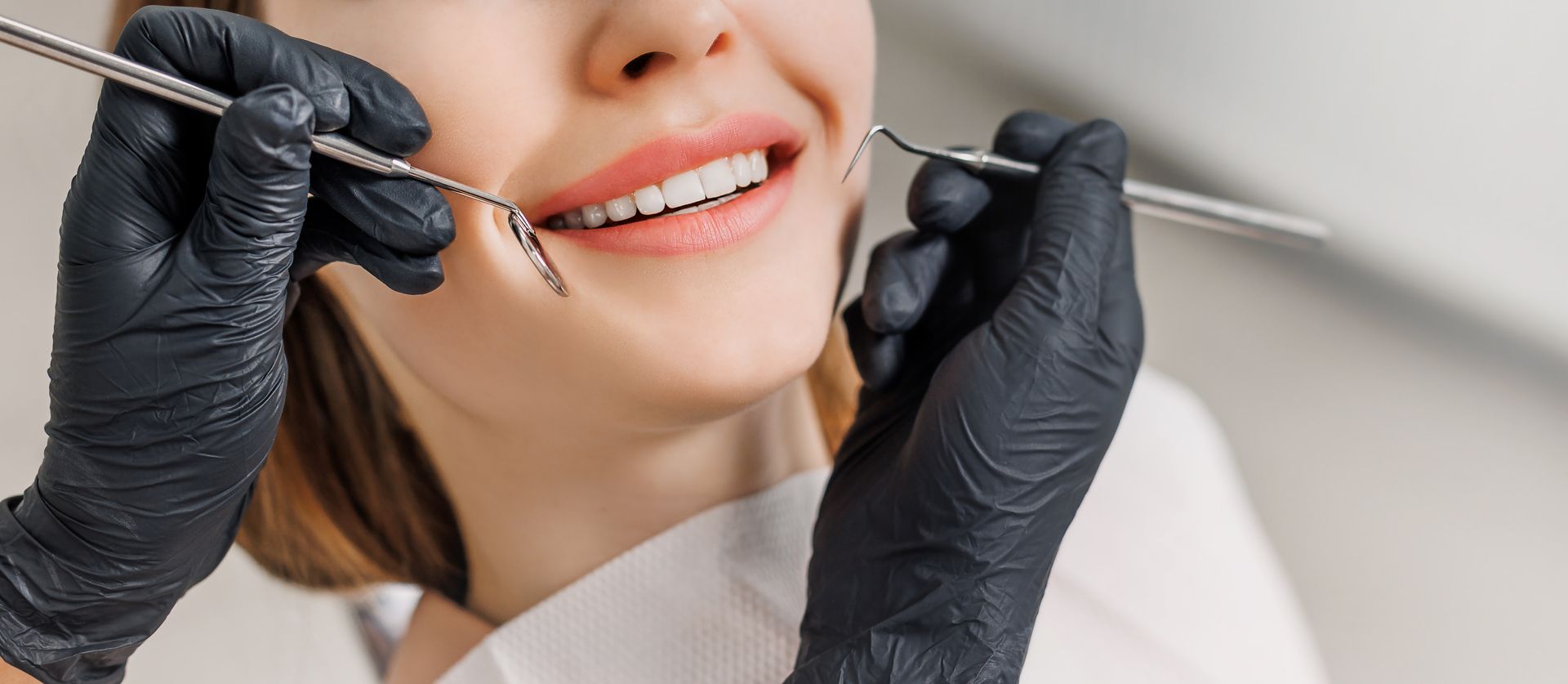Dentist using dental tools to examine a smiling patient’s teeth