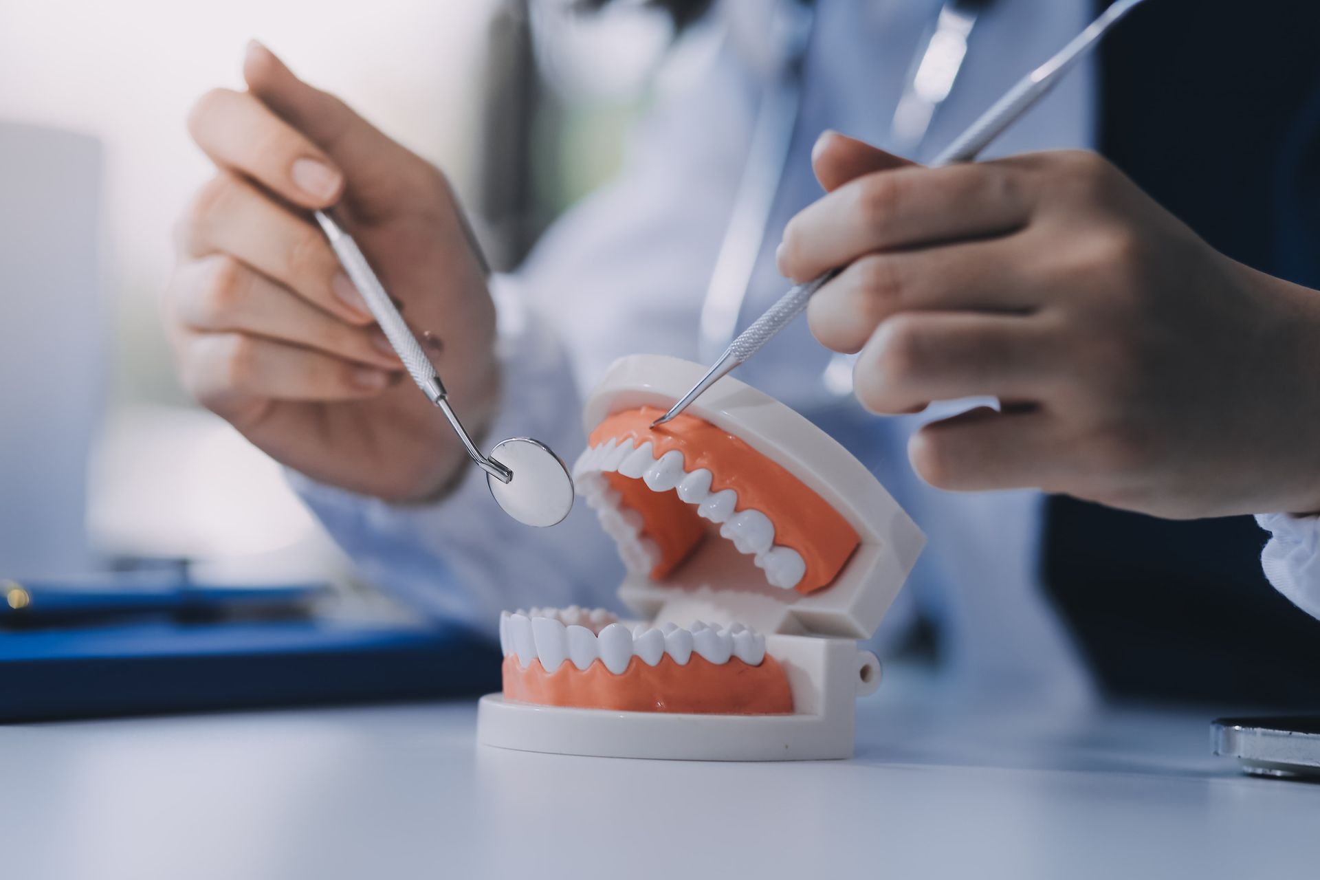 Dentist tools cleaning a dental model with orange gums and white teeth on a table