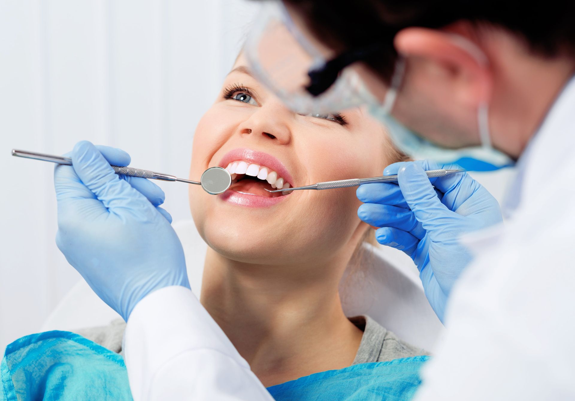 Dentist examining a smiling patient’s teeth with dental tools and blue gloves