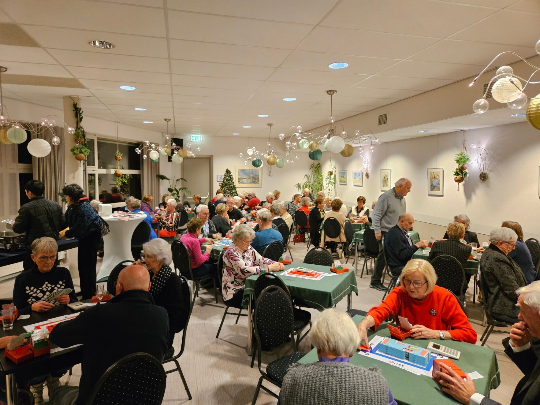 Mensen spelen kaartspelletjes aan tafels in een versierde kamer.