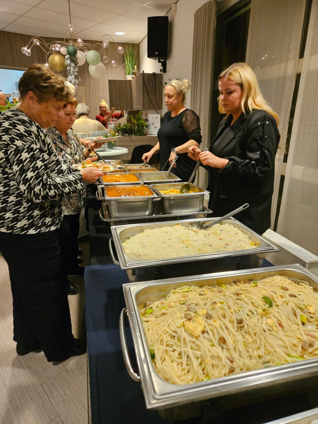 Buffet waarbij mensen zichzelf bedienen. Bedienend personeel staat achter een tafel met warmhoudschalen vol eten.