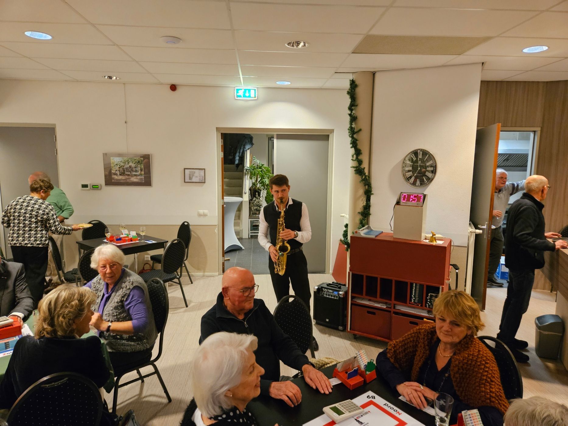 Een saxofonist speelt voor mensen die aan tafels in een zaal zitten. Op de achtergrond staan ​​mensen.