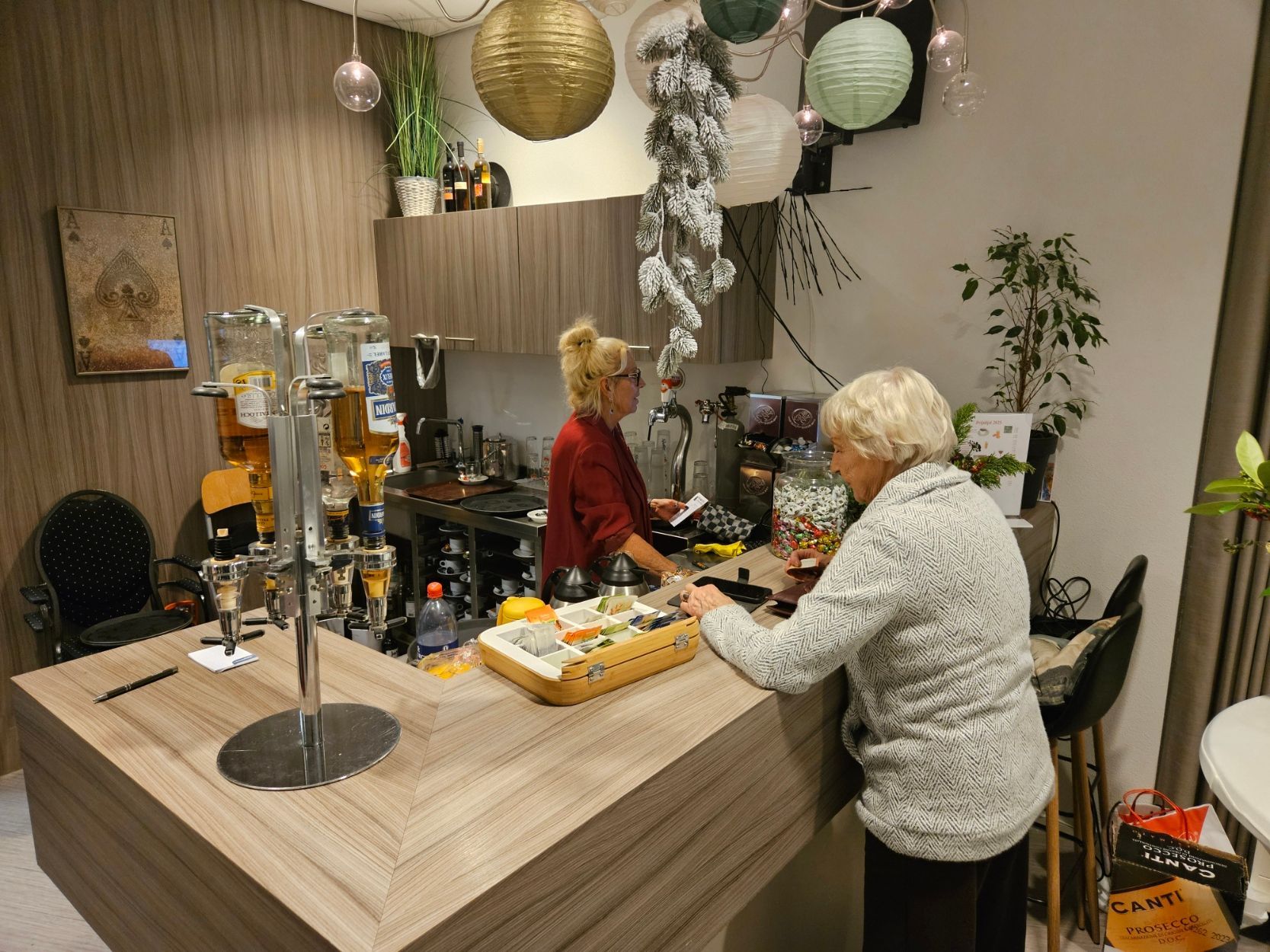 Een persoon staat aan de bar en praat met een barman. Boven hen hangen feestelijke versieringen.