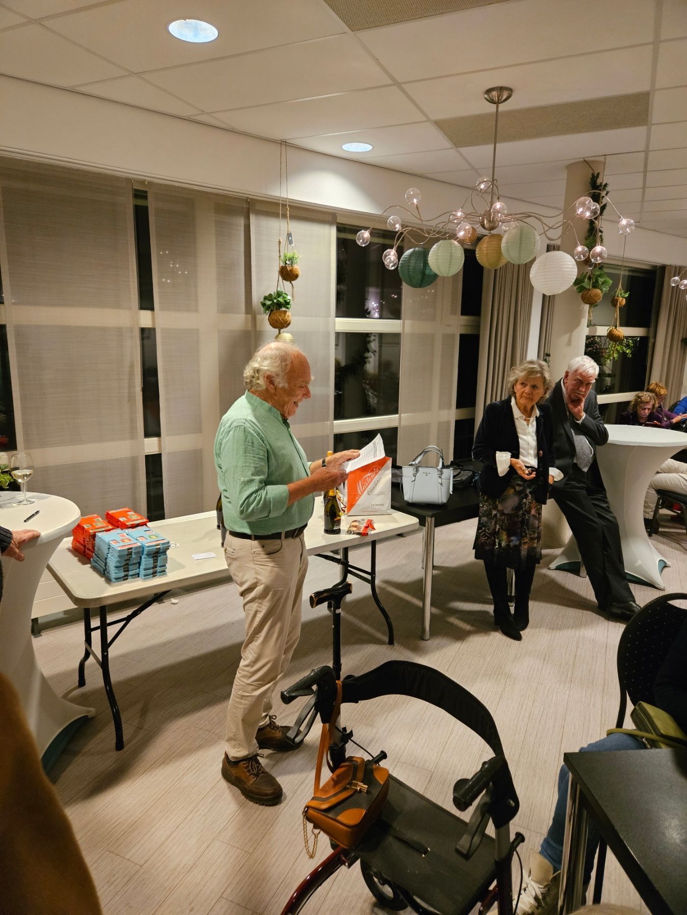 Een man in een groen shirt houdt een toespraak tijdens een bijeenkomst. Andere mensen staan ​​in de buurt.