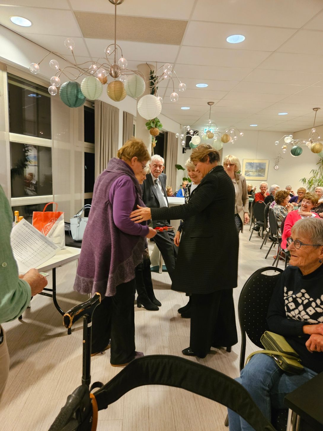 Vrouw in paarse jas ontvangt een prijs, kleine bijeenkomst, zachte verlichting.