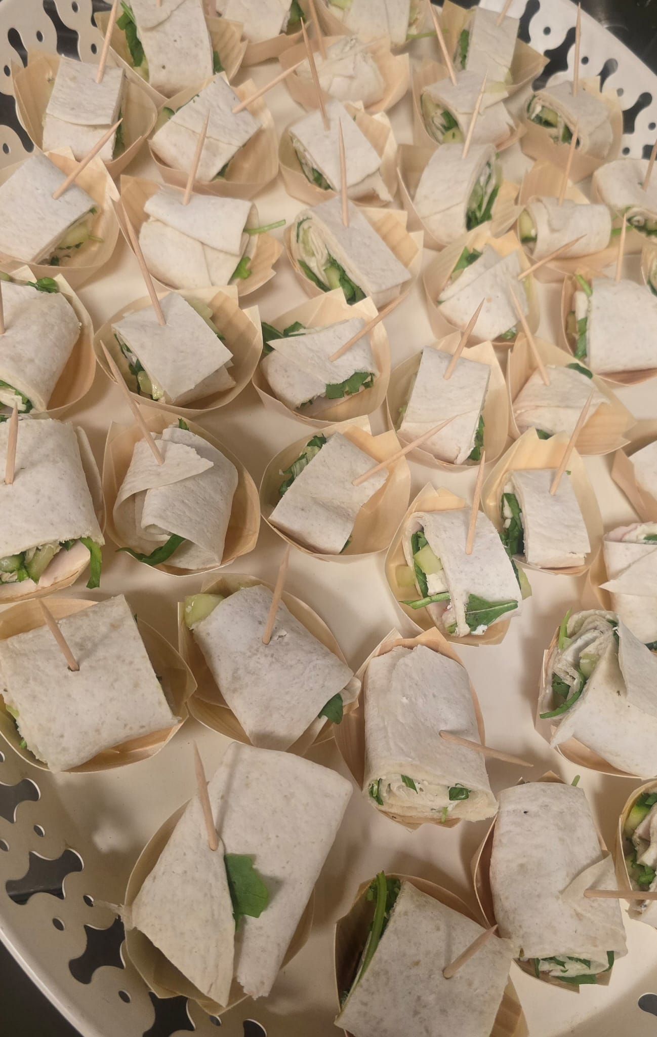 Een schaal met kleine tortillawraps, vastgezet met tandenstokjes, mogelijk als voorgerecht.