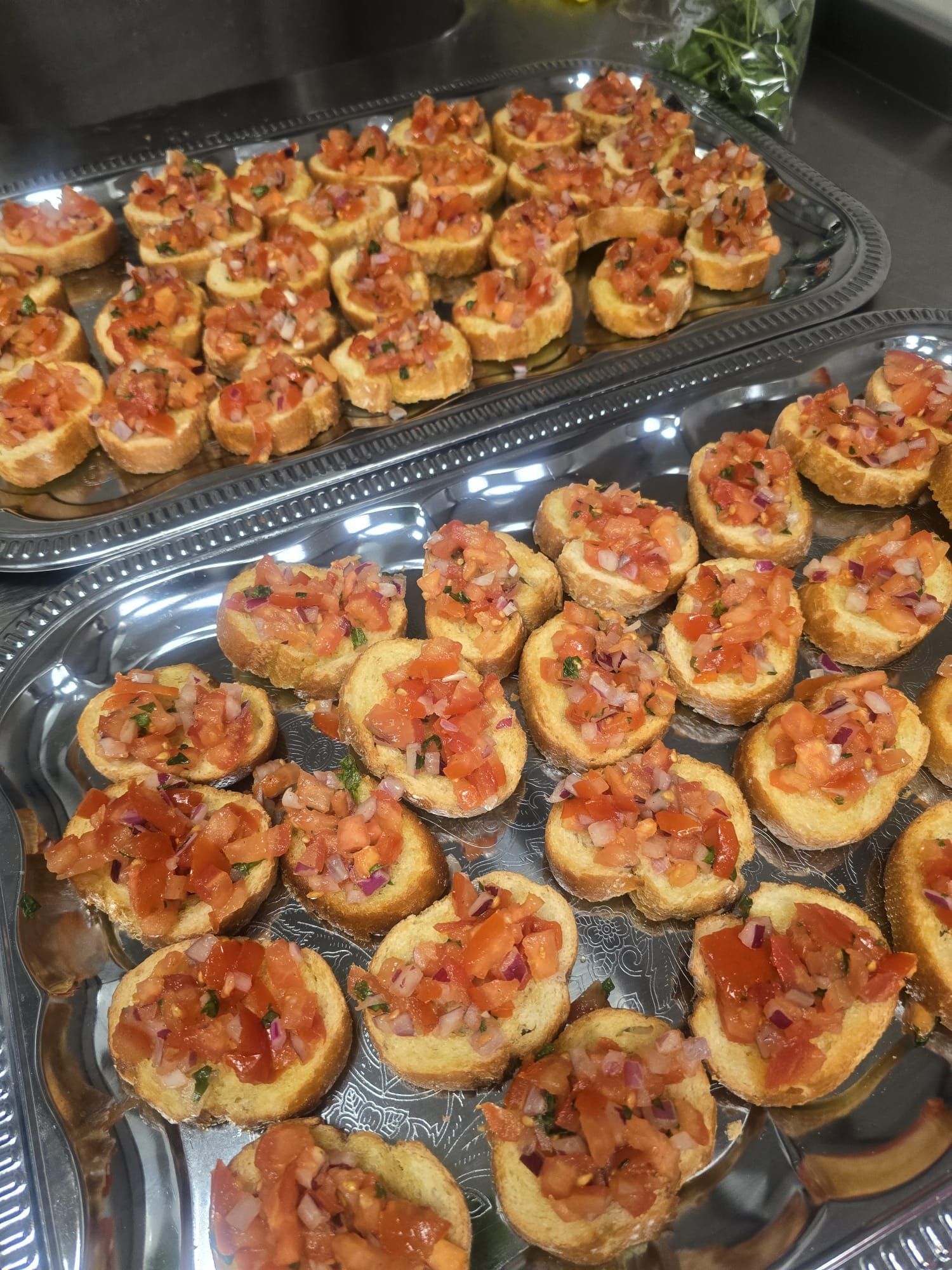 Twee zilveren schalen met bruschetta: geroosterd brood belegd met blokjes tomaat, ui en kruiden.