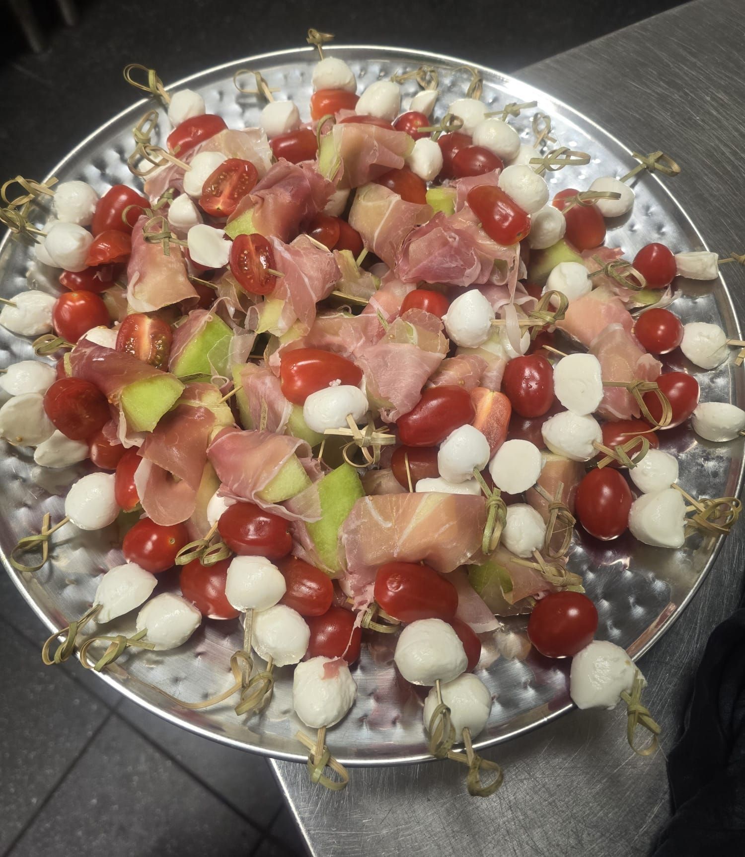 Spiesjes met meloen, mozzarella, tomaten en prosciutto als voorgerecht, geserveerd op een zilveren schaal.