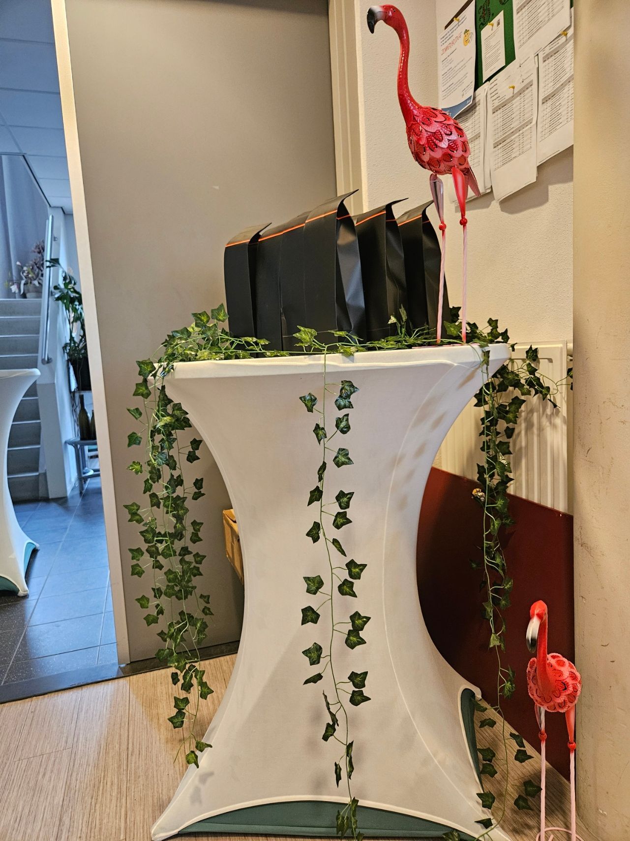 Witte tafel met klimop en zwarte tassen, versierd met roze flamingo's, binnen.
