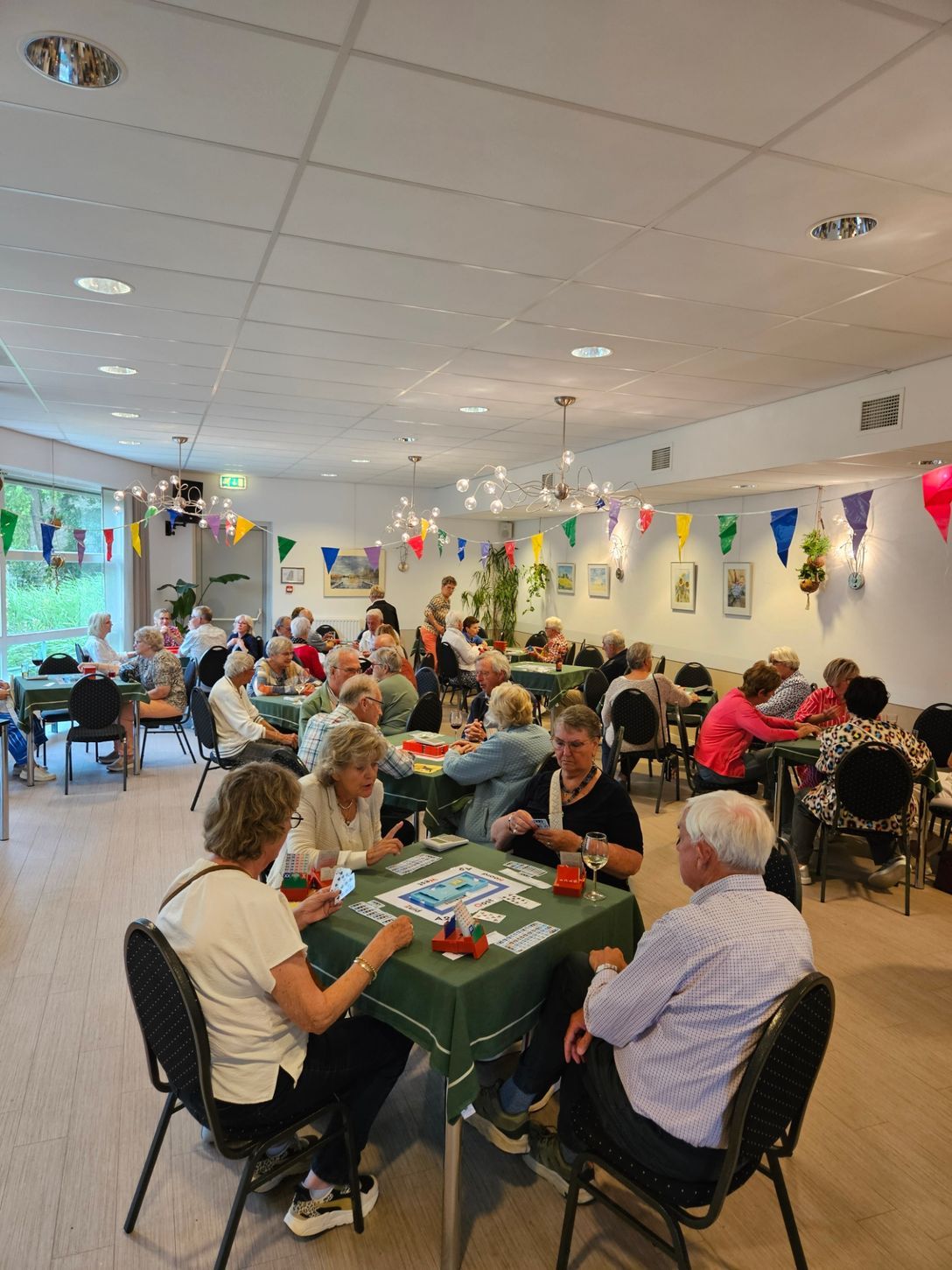 Mensen spelen kaartspelletjes aan tafels in een versierde kamer.