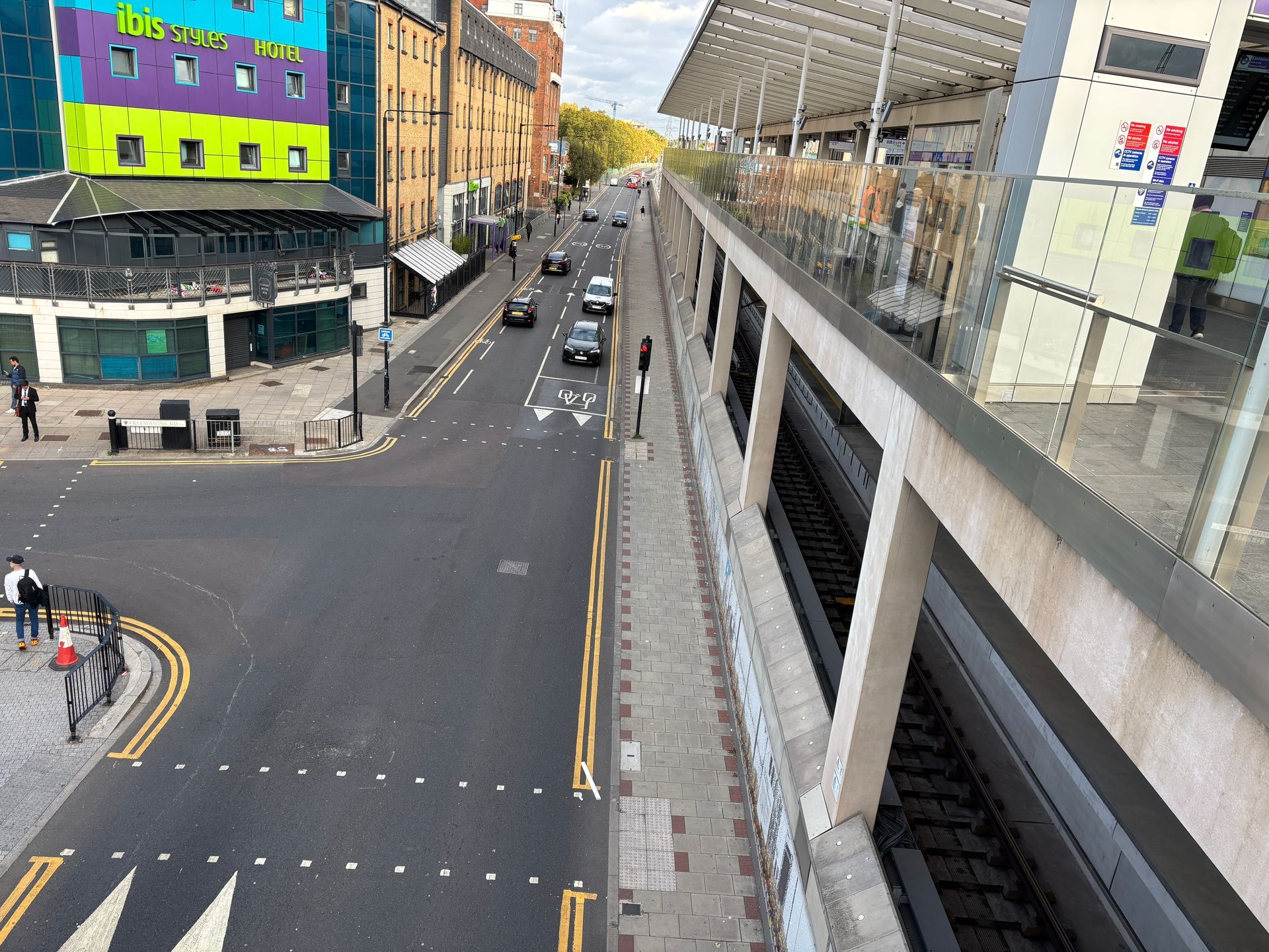 A city street runs parallel to a light rail track, with a vibrant, multi-colored hotel building on the left.