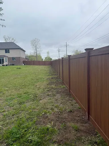 A vinyl fence surrounds a lush green field in front of a house.
