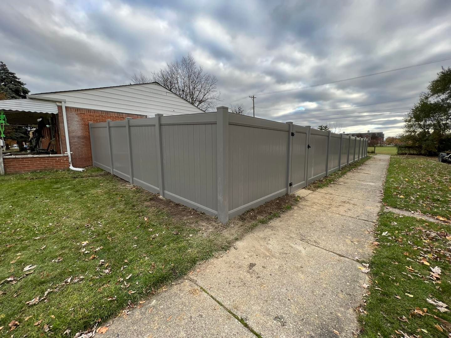 a gray fence along a sidewalk in front of a brick house.