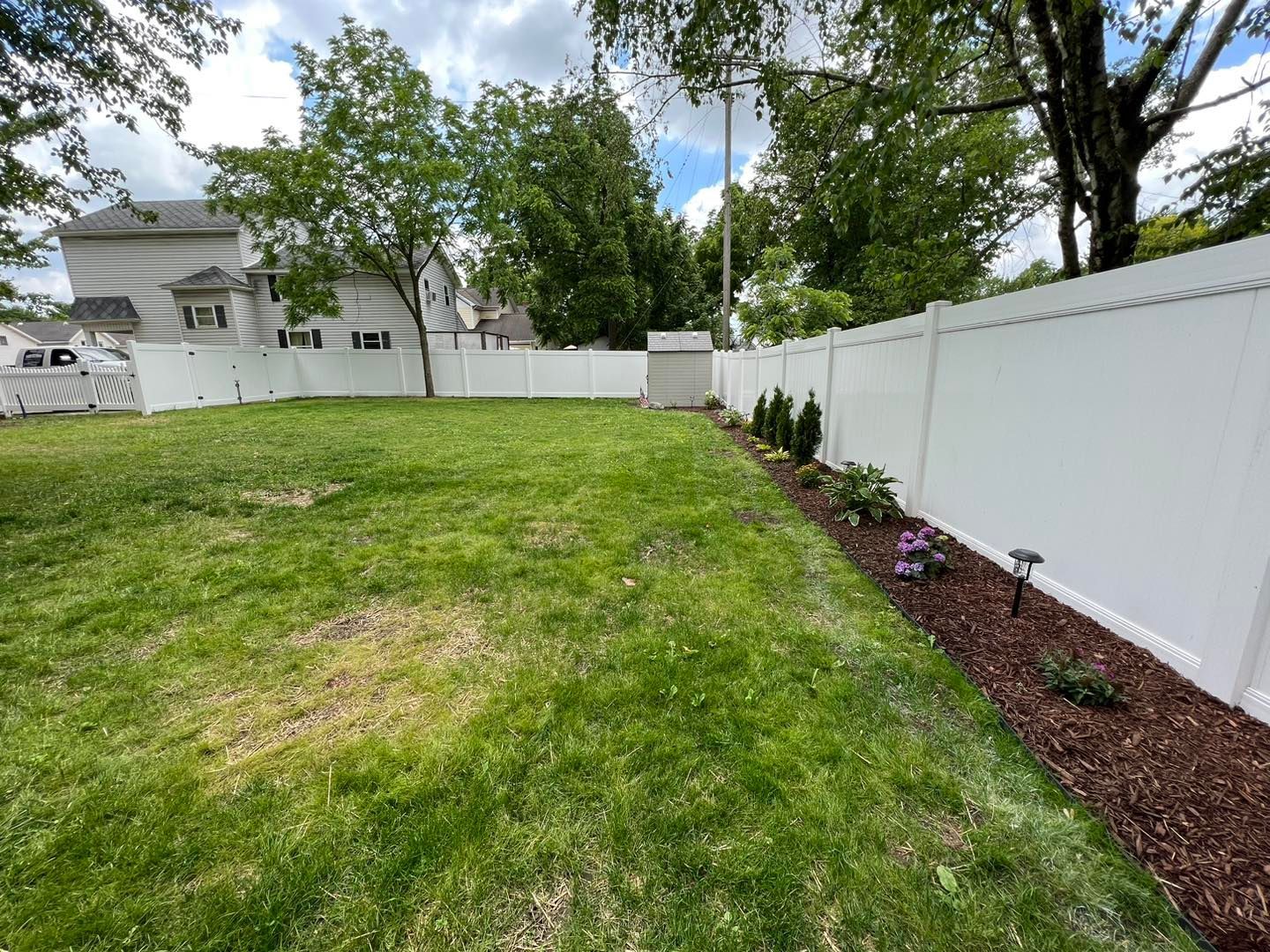 a white fence surrounds a lush green yard with a small garden.