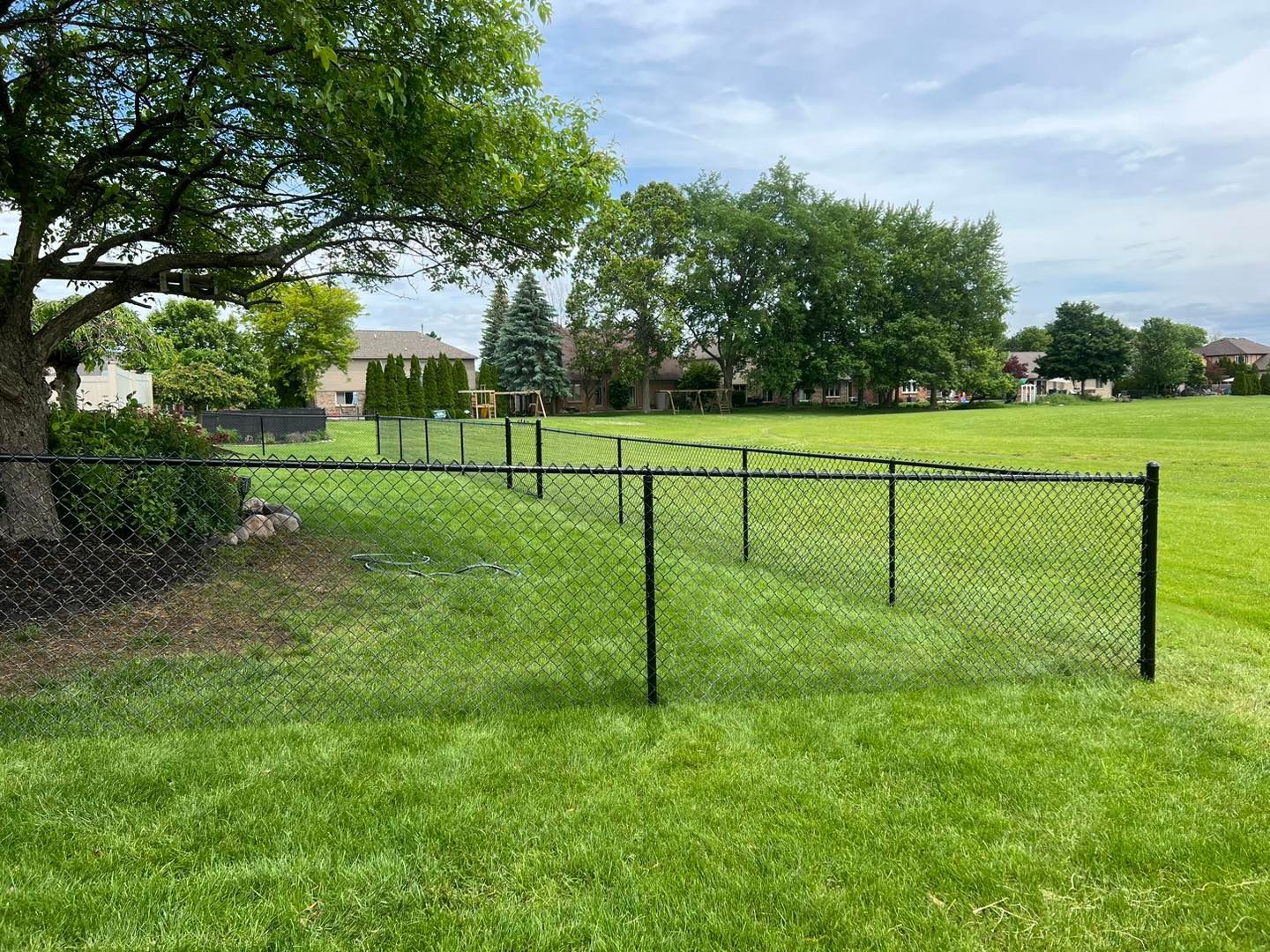 A chain link fence surrounds a lush green field.