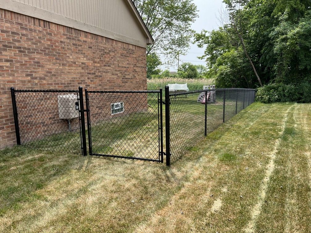A chain link fence with a gate in front of a brick house.