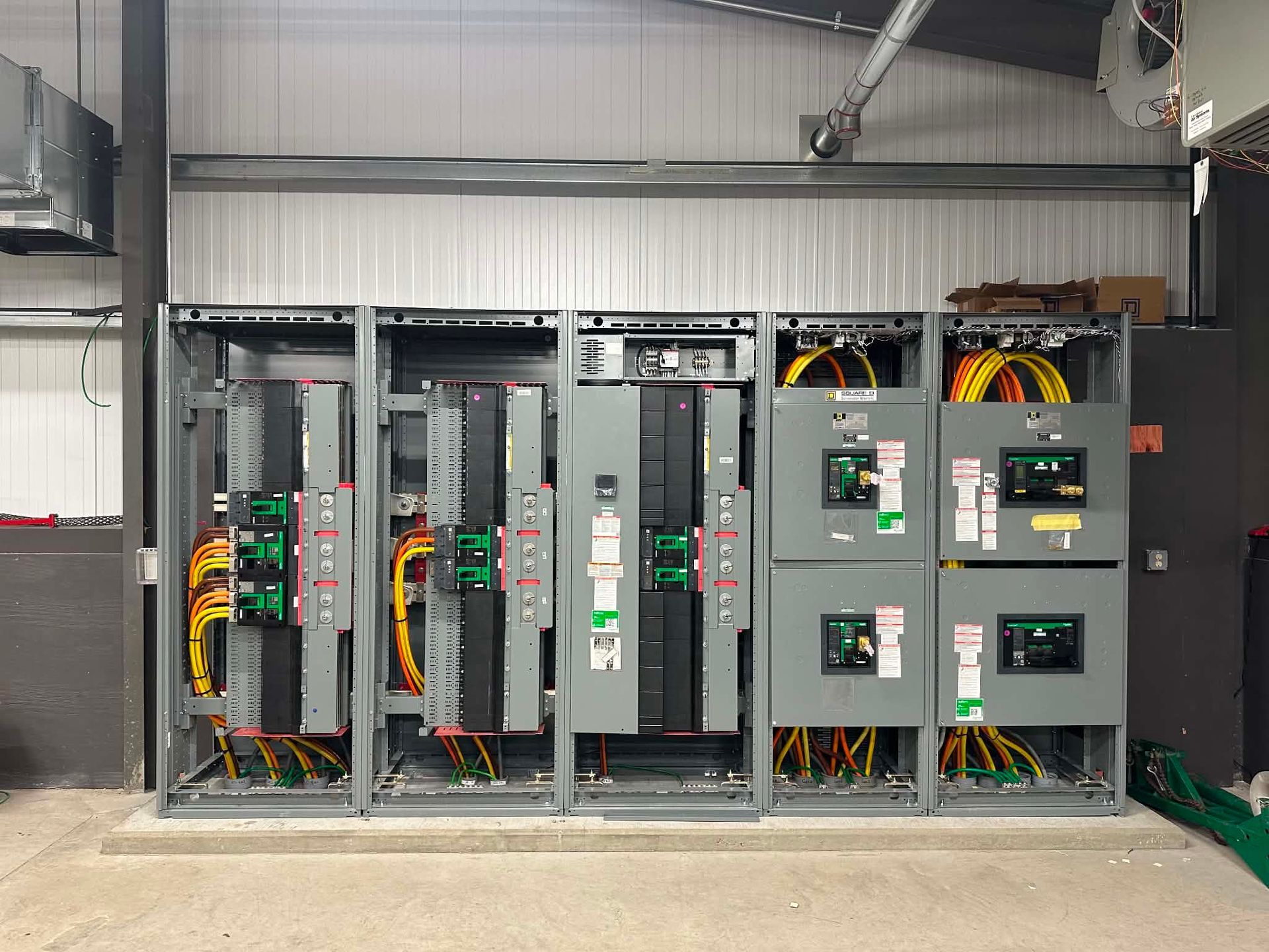 Industrial electrical control panel with open cabinets, wiring, and circuit components in a factory setting