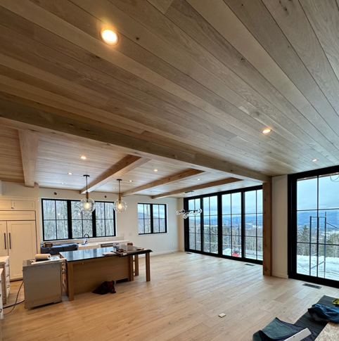 Bright open modern room with wood ceiling, large windows, and a kitchen island under construction