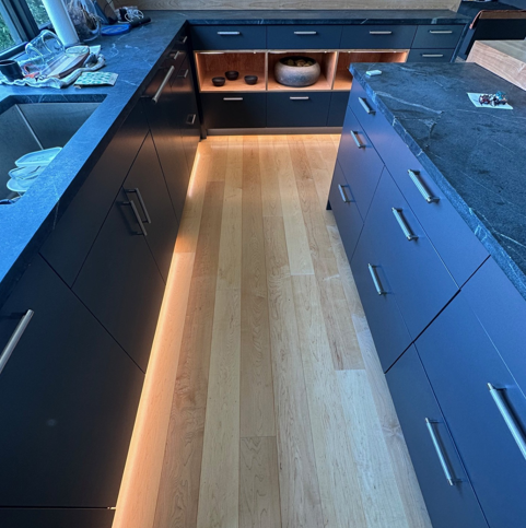Modern kitchen with dark cabinets, wood floor, and a long island countertop with warm under-cabinet lighting
