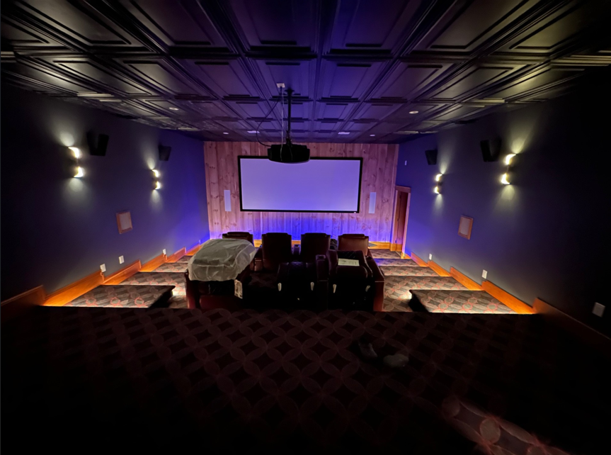 Empty home theater with purple walls, orange floor lighting, and a large projection screen