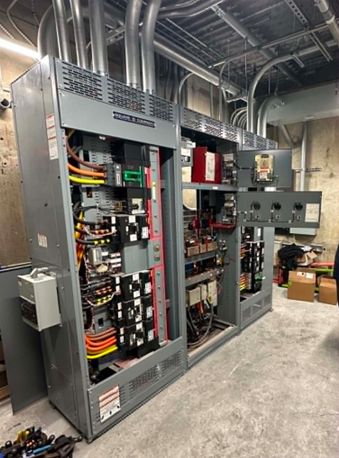Open electrical switchgear panels in an industrial room with exposed wiring and conduit.