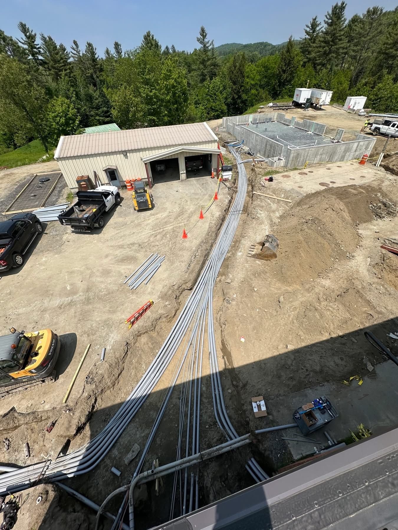 Construction site with heavy machinery, a partially built structure, and a curved retaining wall beside a road.